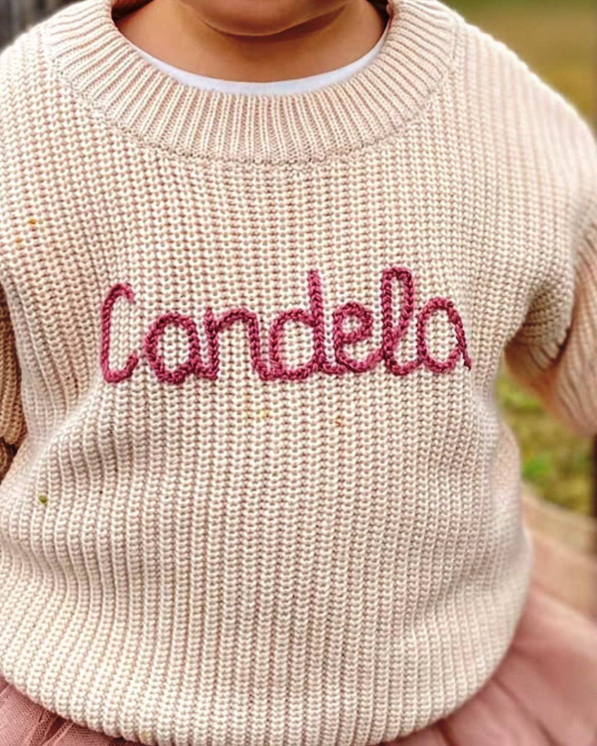 Niña con jersey crudo bordado con su nombre, Candela, en rosa viejo