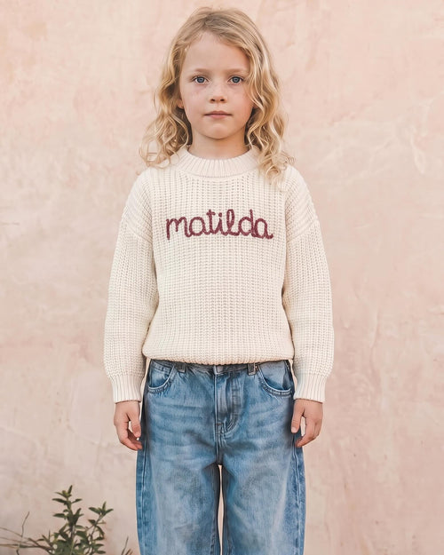 Niña con jersey crudo y el nombre matilda bordado a mano en granate